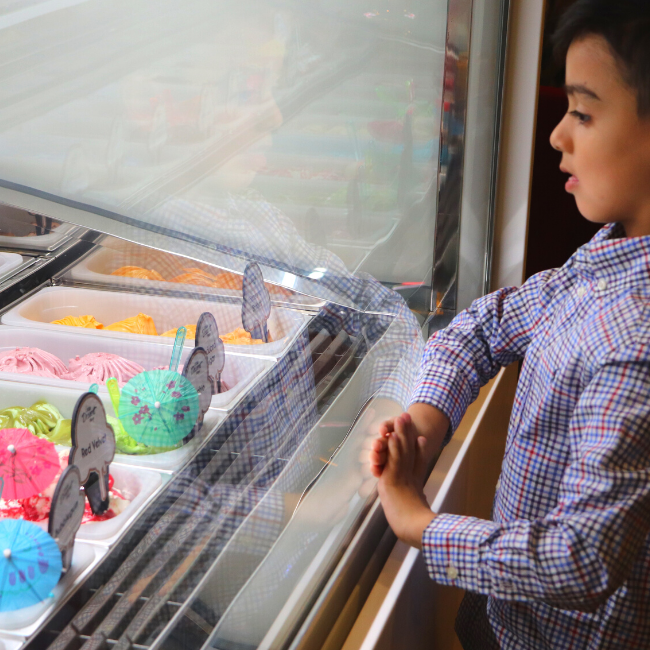 A child deciding which Little Dessert Shop gelato to choose through a glass display